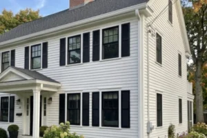 Two-story Colonial-style New England home with dark gutters and multiple downspouts protecting the roofline.
